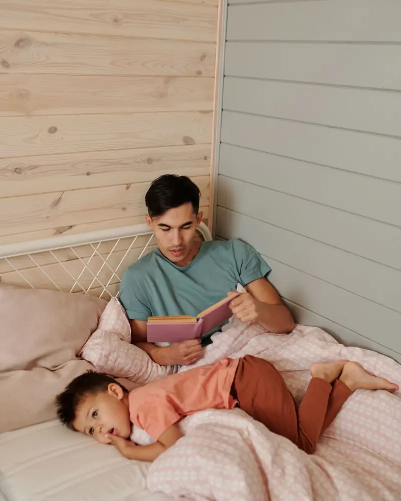 A father reading a book while his young son rests beside him