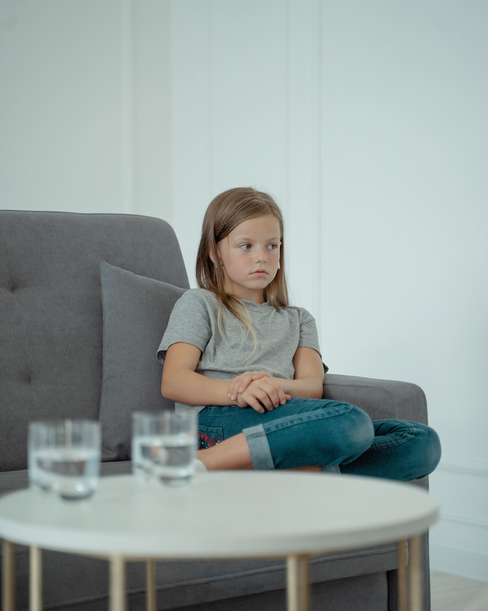 A young girl sitting quietly on a gray sofa