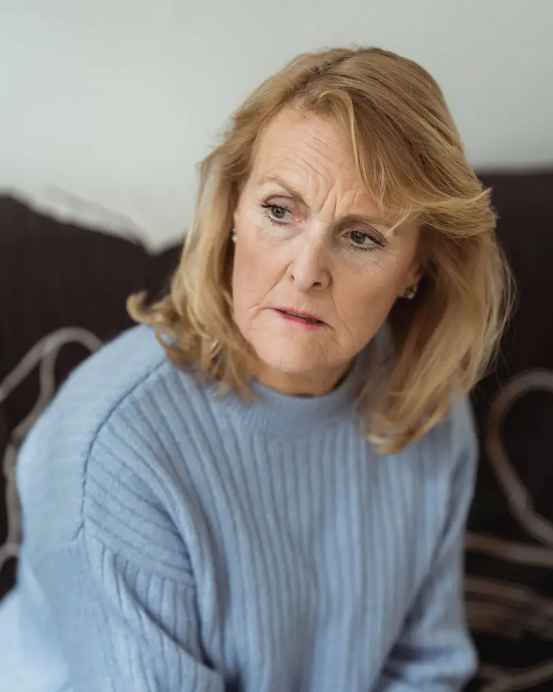 A middle-aged woman in a blue sweater sitting on a couch and looking away