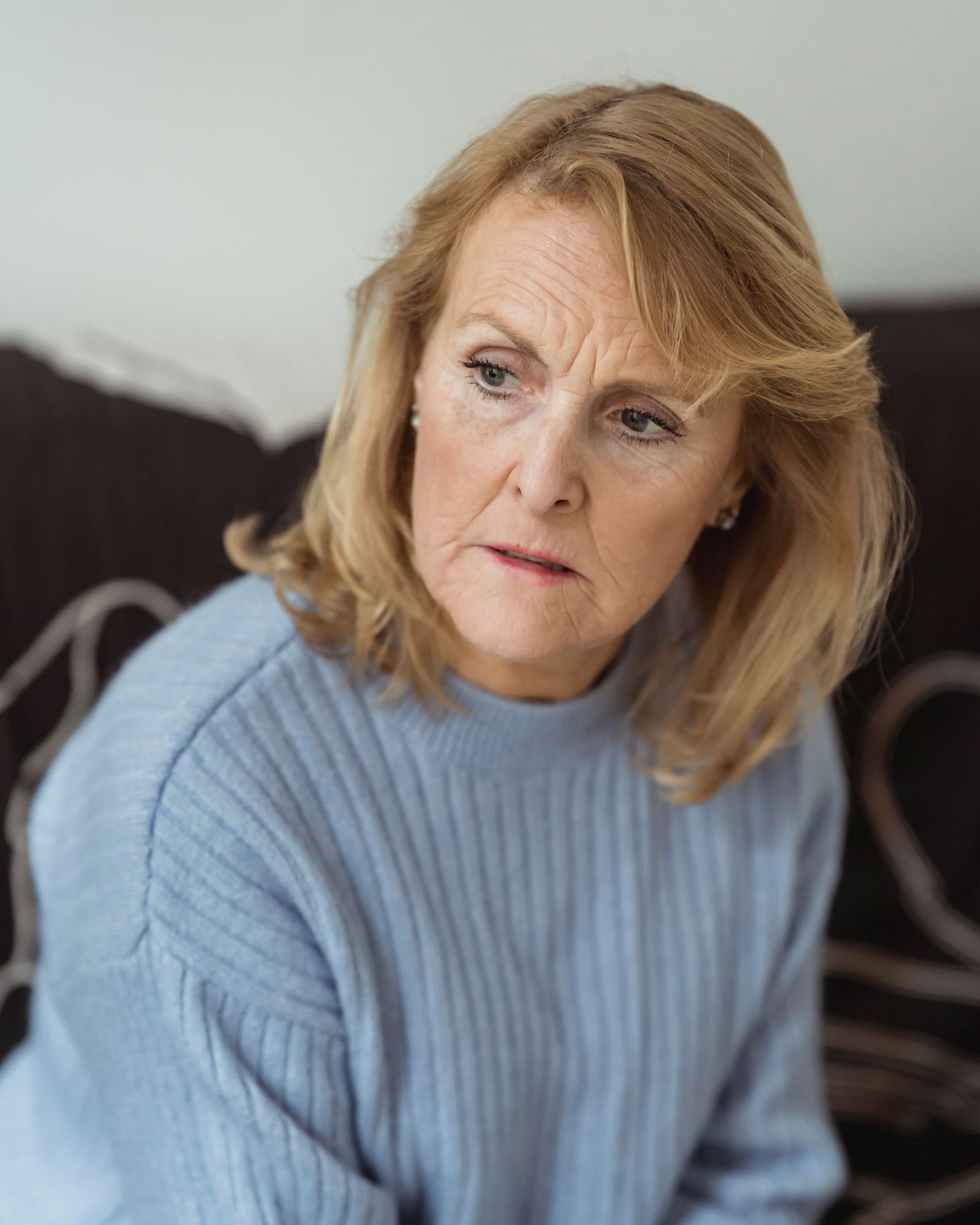 A middle-aged woman in a blue sweater sitting on a couch and looking away
