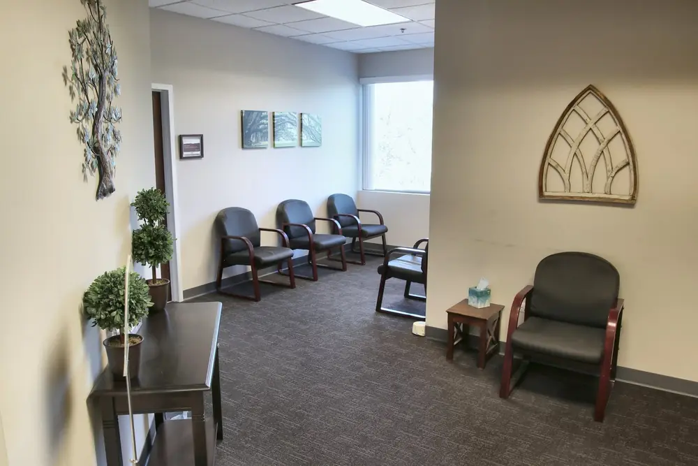 The waiting room at the Geneva office, with dark chairs along the wall, a small table with tissues, potted topiaries, and an arched wall decoration.
