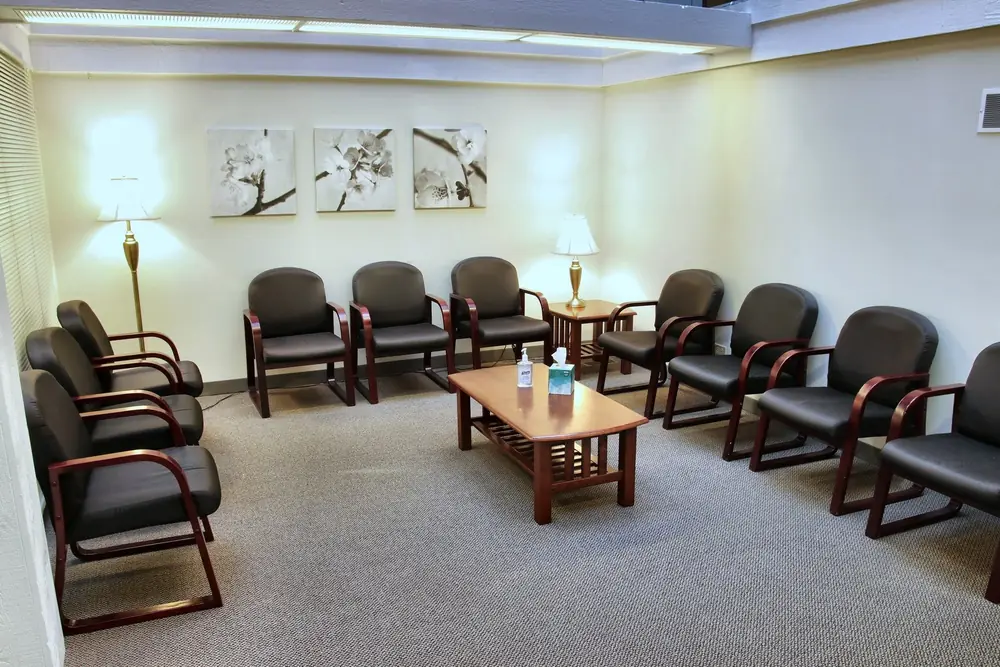 The waiting room at the Naperville office, with rows of dark chairs, a wooden coffee table, two lamps, and floral prints on the wall.