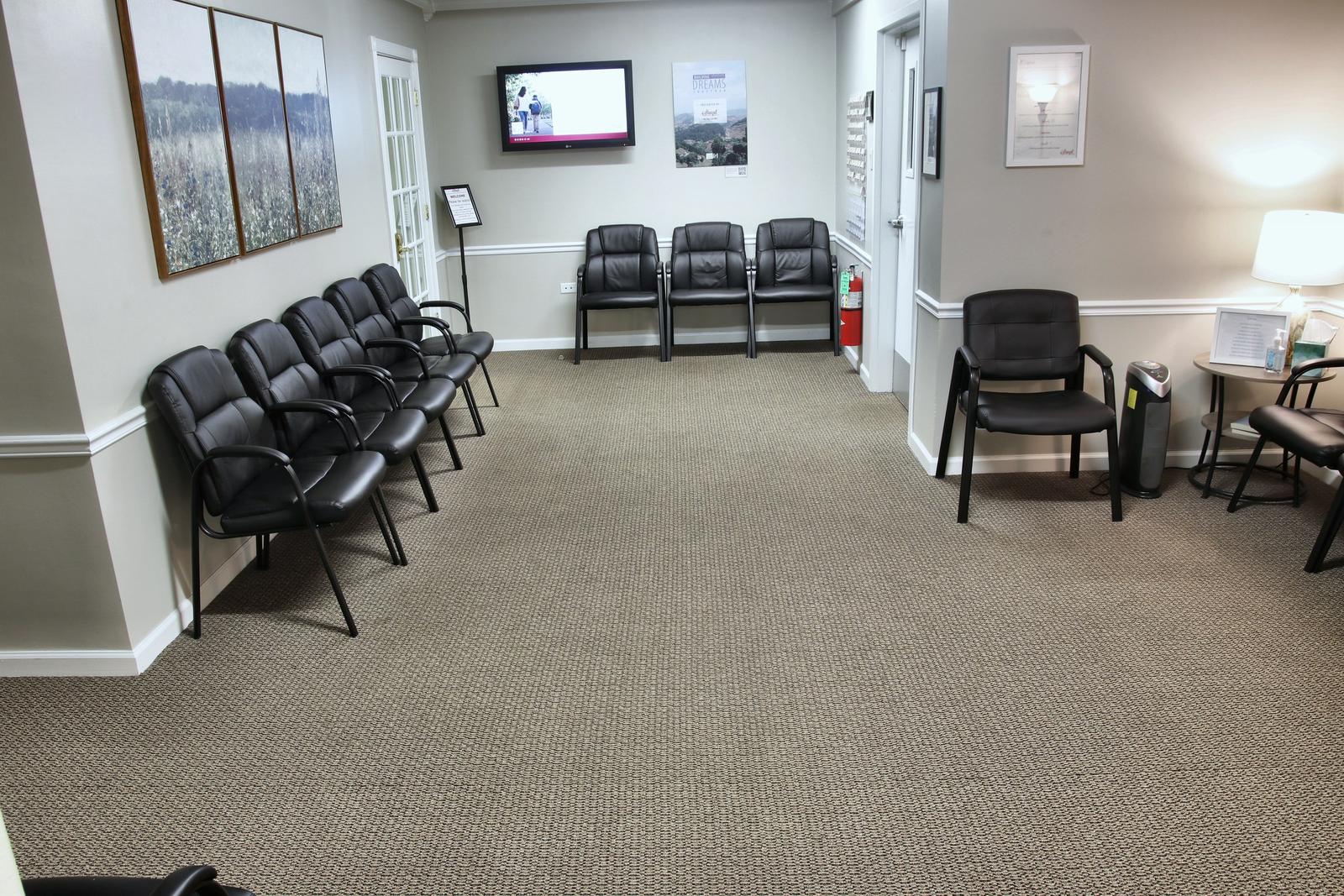 The waiting room at the Wheaton office, with black chairs along the walls, framed meadow prints, and a wall TV.