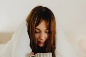 A woman wrapped in a soft blanket, holding a warm mug.