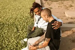 Two friends sitting together on a curb, one with an arm around the other.
