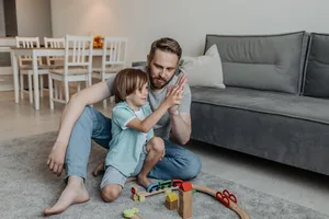A father and his young son playing with a toy train set on the living room rug.