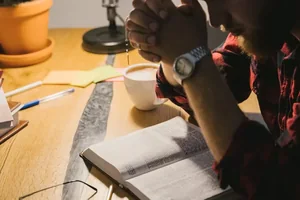 A man praying with his hands folded over an open Bible.