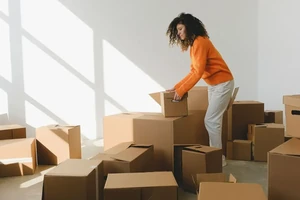A woman unpacking moving boxes in a sunny new room.