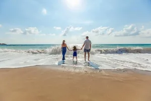 A parent and two children walking hand in hand along the edge of the sea, seen from far behind.
