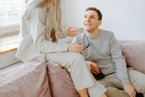 A couple sitting close on a couch, talking and smiling.