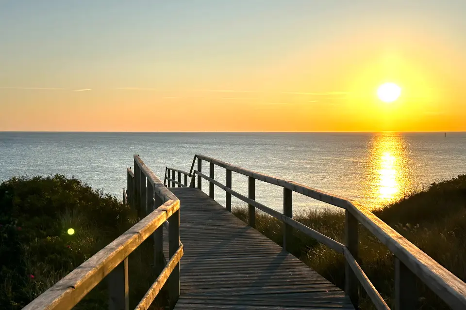 A wooden boardwalk leading toward the sunrise over water.