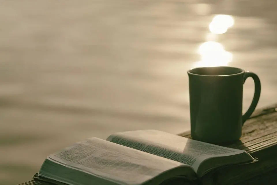 An open Bible and a coffee mug in soft light.