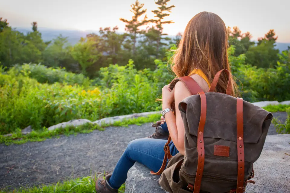 A young person with a backpack resting outdoors, looking at the trees.